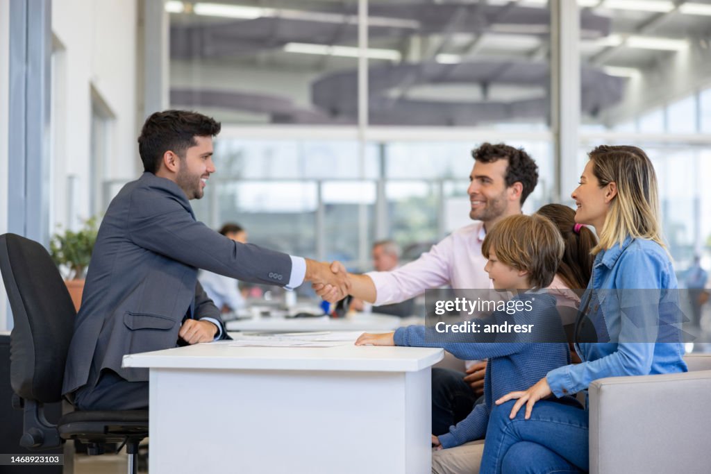 Family closing a deal with a salesman and handshaking while buying a car