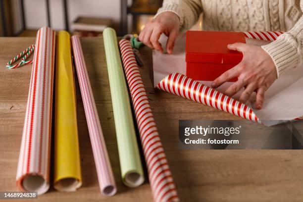 crafty young man measuring how much wrapping paper is going to take to wrap a gift box - roll of wrapping paper stock pictures, royalty-free photos & images
