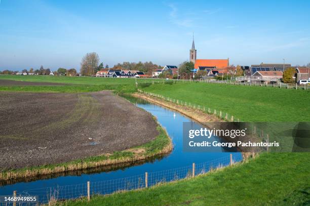 agricultural fields and a canal with a dutch village in the background - noord holland stock pictures, royalty-free photos & images