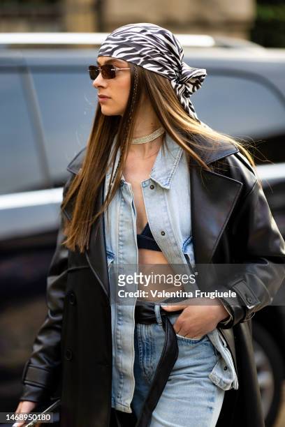 Guest is seen wearing white and black zebra print headscarf, black and silver sunglasses, a diamond choker, a black leather trench, a light blue...