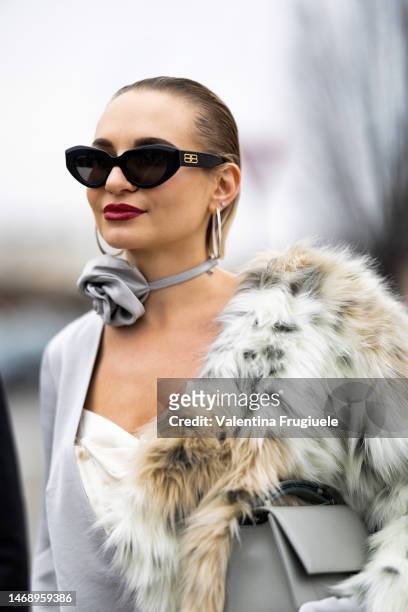 Guest is seen wearing black Balenciaga sunglasses, silver circle earrings, a light grey silk choker embellished with a silk flower, a white long fur...