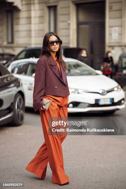 Guest is seen, wearing, an orange shirt, orange matching wide pants, black sunglasses, burgundy red cropped jacket, and beige clutch outside the Max...