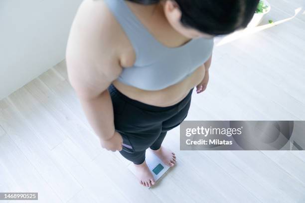 woman standing on weight scale - obesitas stockfoto's en -beelden