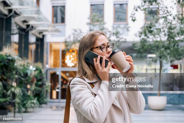 a young woman talking on her smartphone and drinking take-out coffee - disposable cup stock pictures, royalty-free photos & images