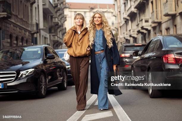 Jeanette Madsen wears a brown zipper jacket, and brown pants and Emili Sindlev wears a navy coat, denim bag, denim shirt, wide leg pants with side...