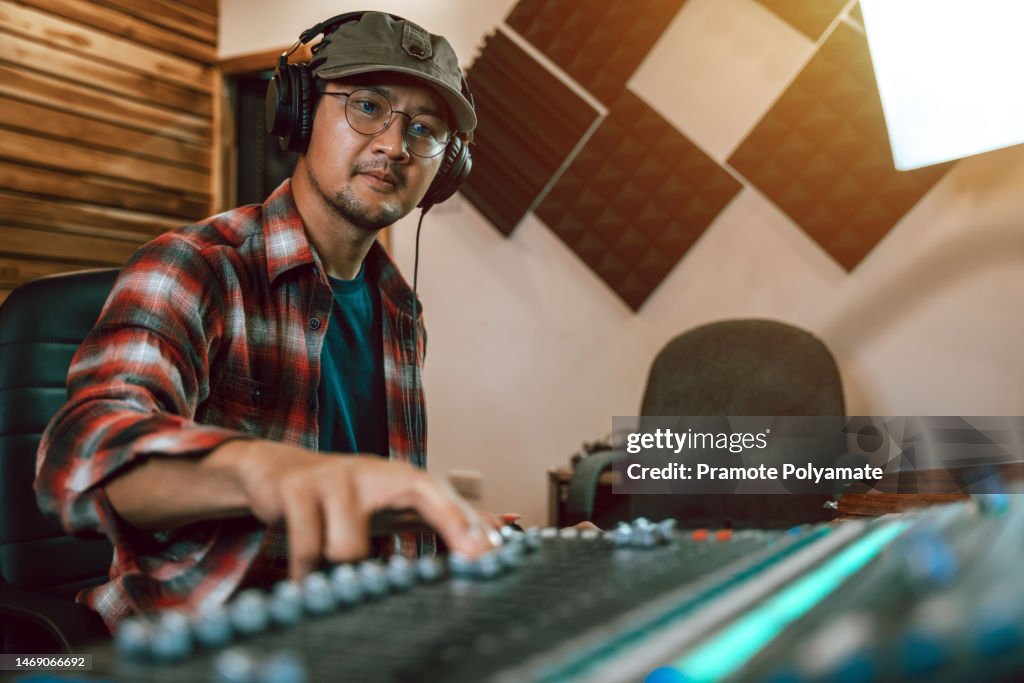 Asian sound engineer working at mixing panel in boutique recording studio. Music production technology.