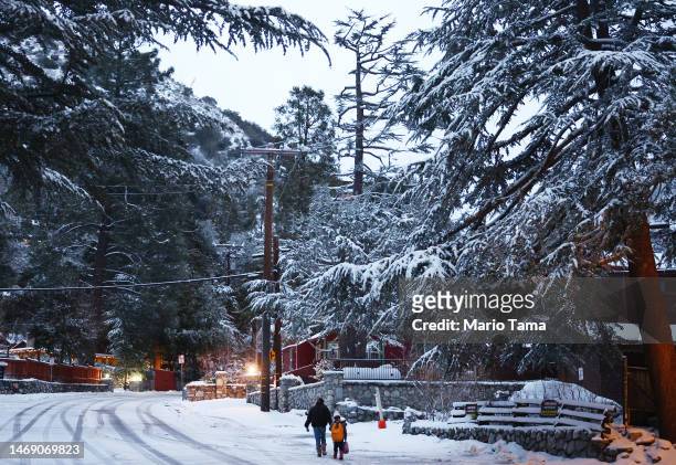 People walk as snow blankets the town in the San Gabriel Mountains, in San Bernardino County along the border of Los Angeles County, on February 23,...