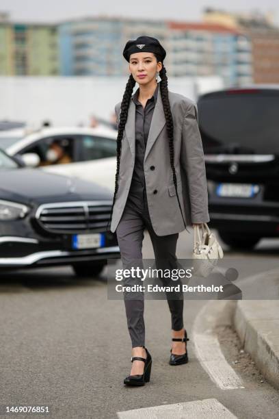 Irene Kim wears a black nylon beret from Prada, a silver triangular pendant earrings from Prada, a black shirt, a pale gray blazer jacket, a gray...