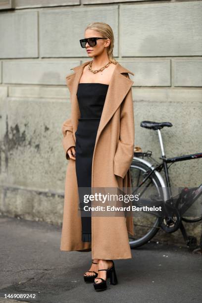 Caroline Daur wears black squared sunglasses, a gold large necklace from Tiffany, a black shoulder-off long midi tube dress, a beige long belted...