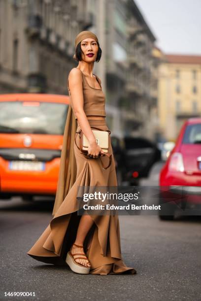 Molly Chiang wears a camel scarf as a headband, a camel square-neck / cropped tank top, a matching camel high waist / ruffled long skirt, a beige...