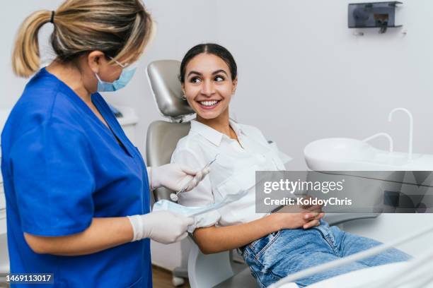 female dentist attending to a smiling young woman - higiene dental imagens e fotografias de stock