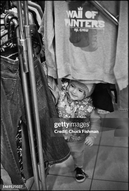 Toddler playing hide and seek in a clothes rack in the JCC Krakow free distribution center for Ukrainian refugees, Krakow, Poland, April 25, 2022.