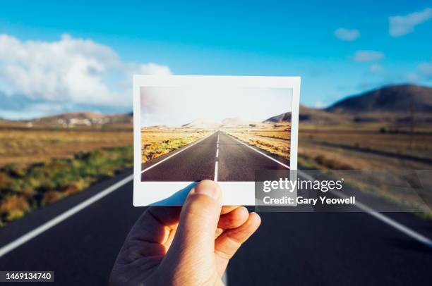 man holding an instant film photo in front of road leading through rugged mountain landscape - wonderlust imagens e fotografias de stock