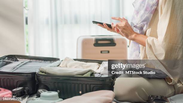 nahaufnahme einer jungen asiatischen muslimischen frau, die einen koffer vorbereitet, verwendet smartphone-checklistenzubehör im schlafzimmer zu hause. reiseurlaub. - lost luggage stock-fotos und bilder
