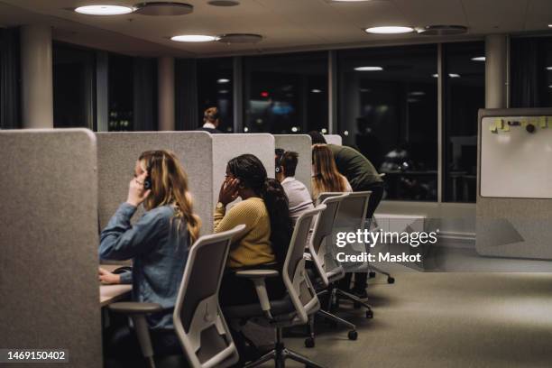 multiracial team working side by side in illuminated call center - callcenter stock-fotos und bilder