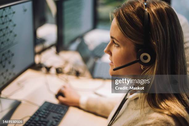 side view of female customer service representative talking through headset at call center - hotline stock-fotos und bilder