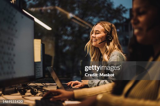 Cheerful young female customer service representative working by colleague at desk in call center Cheerful young female customer service representative working by colleague at desk in call center
