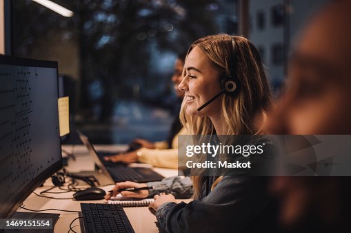 Smiling blond female customer service representative wearing headset using computer at desk in call center