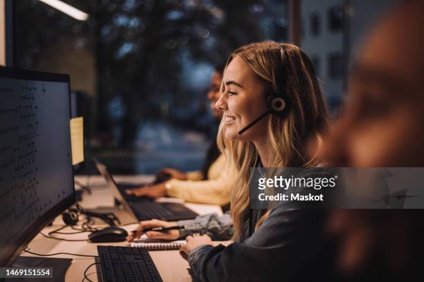 smiling blond female customer service representative wearing headset using computer at desk in call center - customer experience stock pictures, royalty-free photos & images