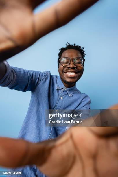 happy black man having fun while taking a selfie against blue background. - men selfie wide stock pictures, royalty-free photos & images