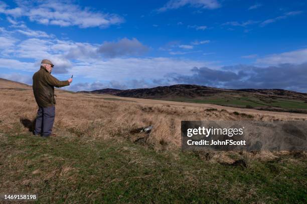 senior man in a rural scene looking at his mobile phone - waxed jacket stock pictures, royalty-free photos & images