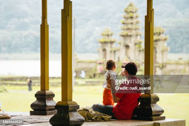 asia, indonesia, bali, asian family sitting inside pavillion  enjoy the travel, in front of tamblingan water temple, while sightseeing. - indonesia family stock pictures, royalty-free photos & images