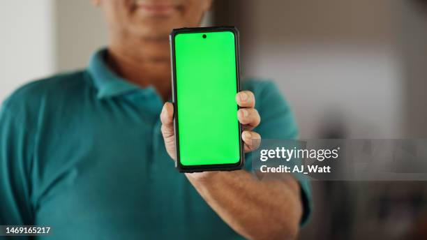 lächelnder reifer mann, der ein smartphone mit grünem bildschirm hochhält und zeigt - hochhalten stock-fotos und bilder
