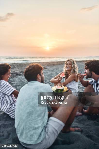cheerful couples talking while eating fruit on the beach at sunset. - picnic imagens e fotografias de stock
