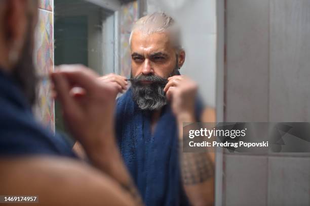 confident young man in front of bathroom mirror stretching his mustache - mirror steam stockfoto's en -beelden