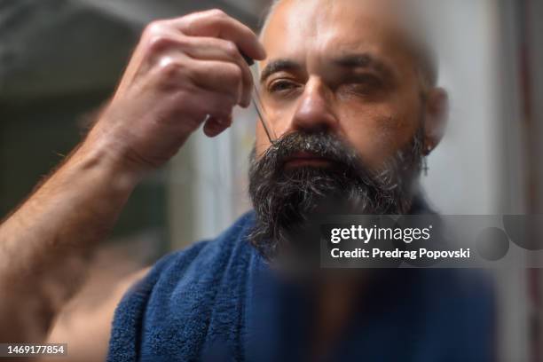 young man applying beard oil in bathroom - face oil stock pictures, royalty-free photos & images