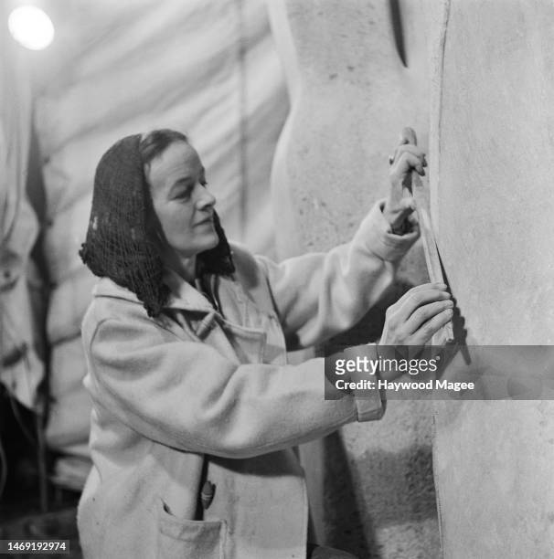 English artist and sculptor, Barbara Hepworth uses a large file to work on her abstract stone sculpture, 'Contrapuntal Forms', at her home, Trewyn...