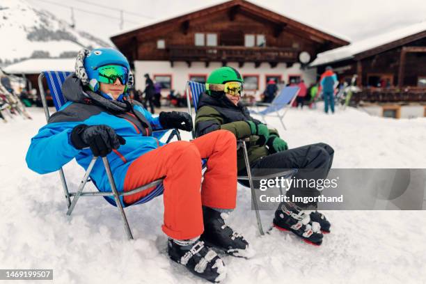 teenage boys enjoying a break in skiing - sitting on sun beds and looking at view. - ski resort stock pictures, royalty-free photos & images