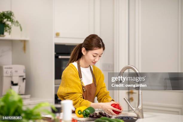 young asian woman washing vegetables in kitchen sink - pepper spray stockfoto's en -beelden