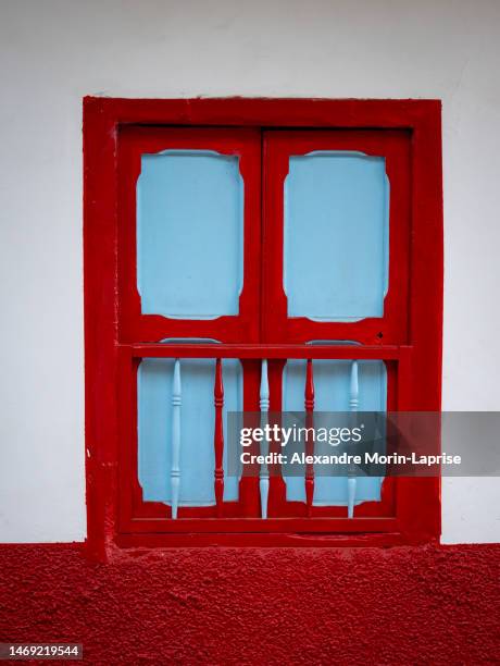 red and cyan window and a white with red background, characteristic of the town of jericho, antioquia, colombia - antioquia stockfoto's en -beelden