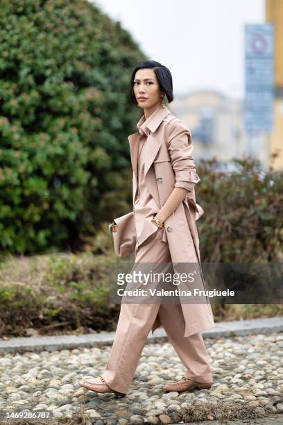 Molly Chang is seen wearing gold long earrings, gold bracelets, a light-beige monochrome look made of a long trench, a shirt and relaxed fit, suit...