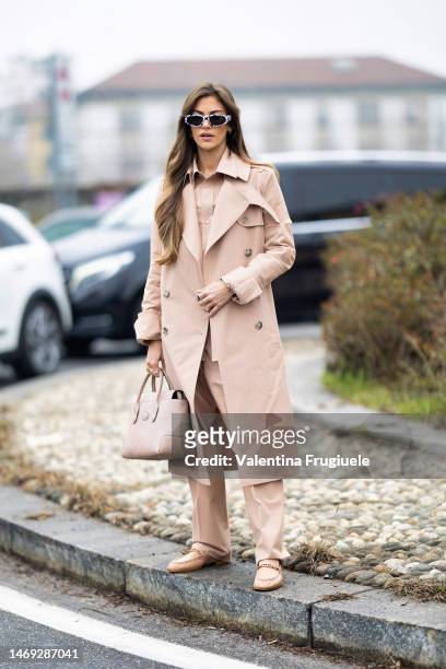 Clara Berry is seen wearing black and white sunglasses, a black and silver ring, gold rings, a light-beige monochrome look made of a long trench, a...