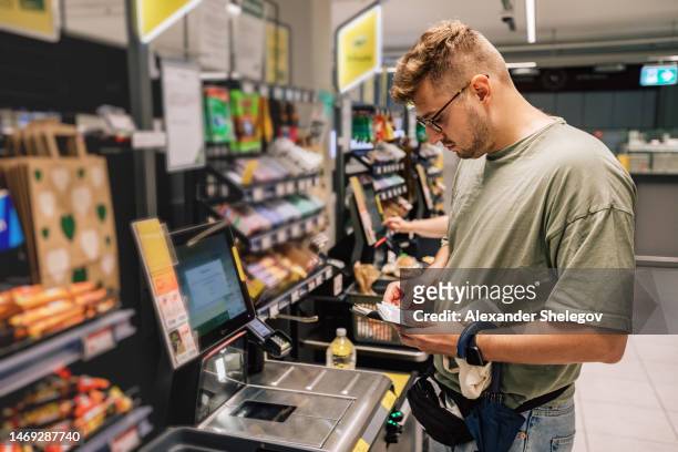 man buying and paying money in the supermarket. photo with people in the store during the shopping. person is using contactless payment - paying supermarket stock pictures, royalty-free photos & images