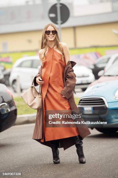 Xenia Tchoumitcheva wears a brown wrapped dress with slit, coat, and beige bag outside Tods during the Milan Fashion Week Womenswear Fall/Winter...