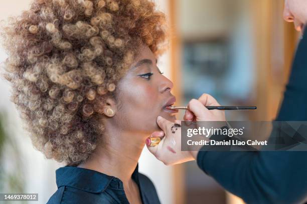 makeup artist applying lipstick with makeup brush on the lips of a young woman. - model backstage stock pictures, royalty-free photos & images