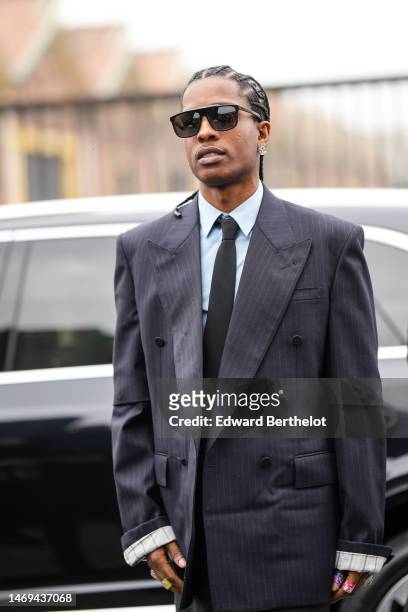 Asap Rocky wears black sunglasses, a white shirt, a black tie, a black striped print pattern oversized blazer jacket, a gray slit / split long skirt,...