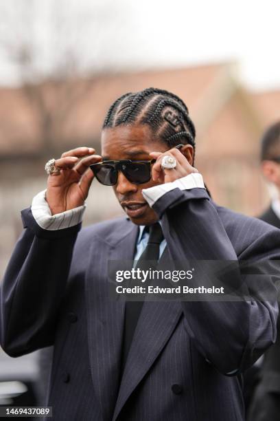 Asap Rocky wears black sunglasses, a white shirt, a black tie, a black striped print pattern oversized blazer jacket, outside Gucci, during the Milan...