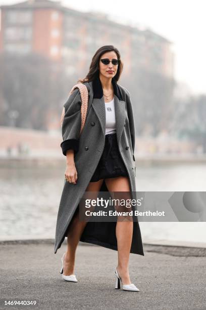 Bettina Looney wears black sunglasses, a gold pendant necklace, a white tank-top from Loewe, a gray with black collar long wool coat, a beige braided...