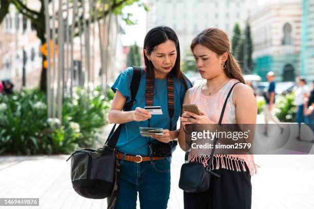 two asian female  traveler having problem paying online with credit card while waiting for a e-hailing ride to pick her up. - malaysia kuala lumpur merdeka square stock pictures, royalty-free photos & images