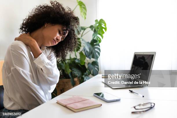 african american woman suffering from neck pain. hispanic female working with laptop at home self massaging neck and shoulders. - human vertebra - fotografias e filmes do acervo