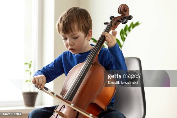 niño blanco de 5 años aprendiendo a tocar el violonchelo - instrumento de cuerdas fotografías e imágenes de stock