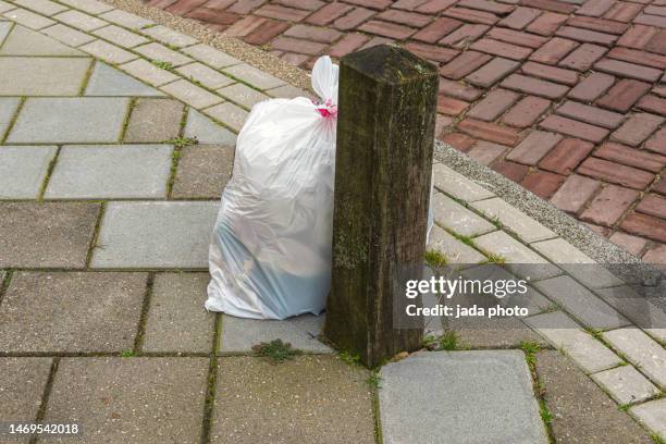 dense white plastic garbage bag on the sidewalk - bin bag stock pictures, royalty-free photos & images