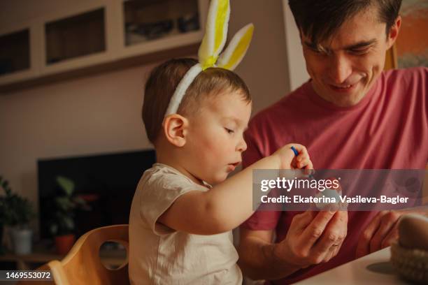 dad and child in bunny ear headbands decorating eggs for easter - easter egg decorating stock pictures, royalty-free photos & images