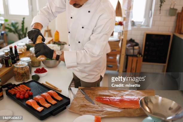 junger profikoch würzt lachs während der zubereitung auf einem elektrogrill in einer heimischen küche - lachssteak stock-fotos und bilder