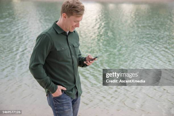 young man uses phone next to canal water - free download photo stock pictures, royalty-free photos & images