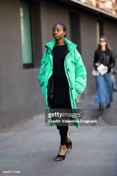 Guest is seen wearing gold earrings, a puffy bright green oversized maxi long winter jacket with black details, a black maxi long dress and black...